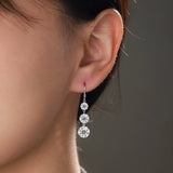 Moissanite drop earrings on ear, three round stones cascading from hook, white gold vermeil