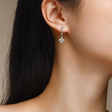 Four-petal moissanite flower drop huggie earrings on model ear, silver-tone