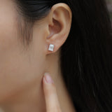 Emerald cut moissanite stud earrings on ear; white gold vermeil setting