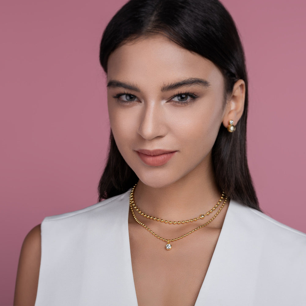Model wearing double-layer beaded necklace set with round blue gem pendant, yellow gold