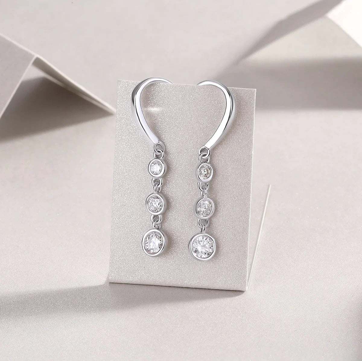 Three-stone moissanite drop earrings with round bezels and lever hook, white gold vermeil