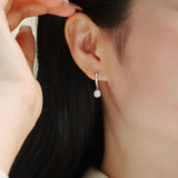 Round moissanite bezel drop earring on ear, polished white-gold tone