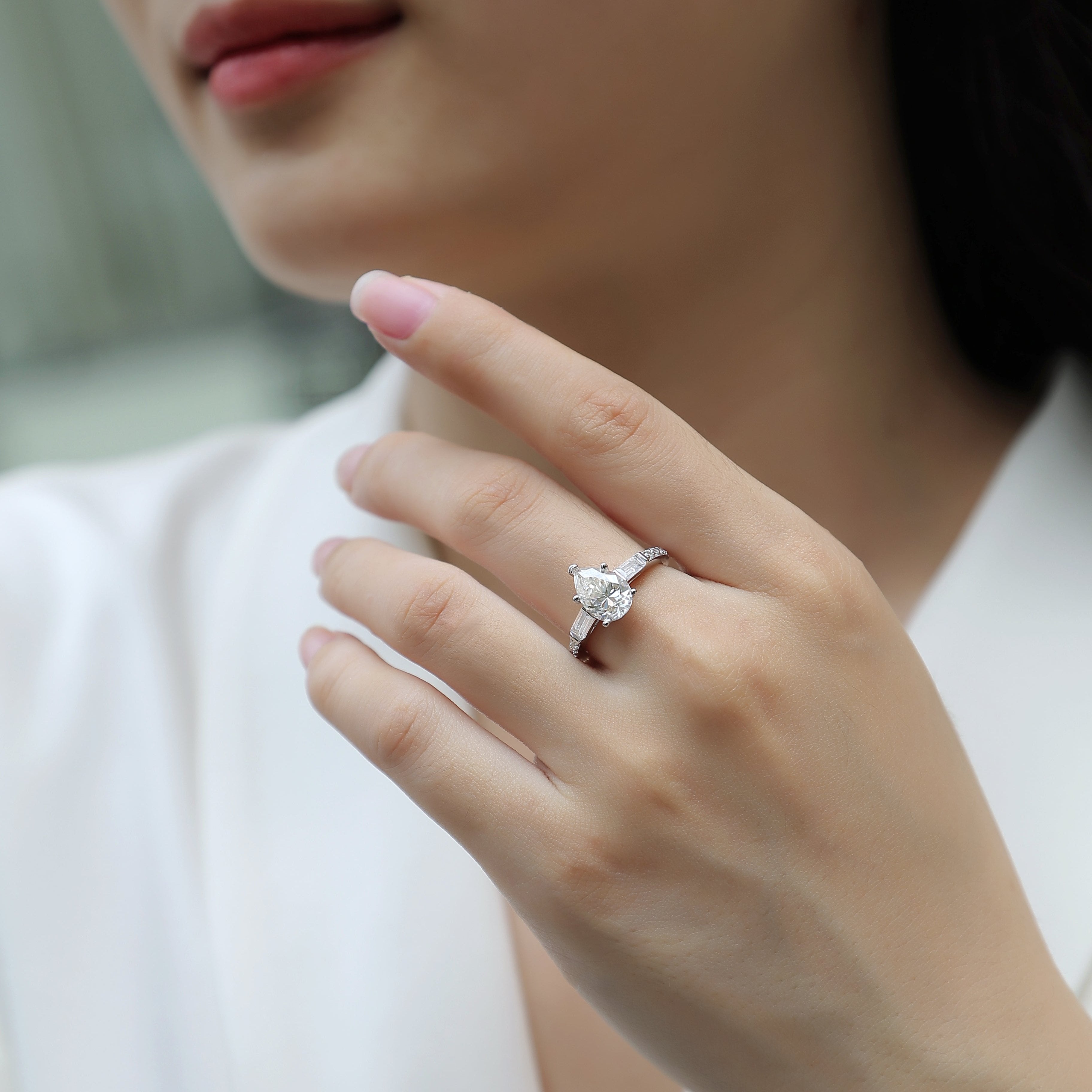 Moissanite engagement ring on hand, pear center with baguette sides and pavé band