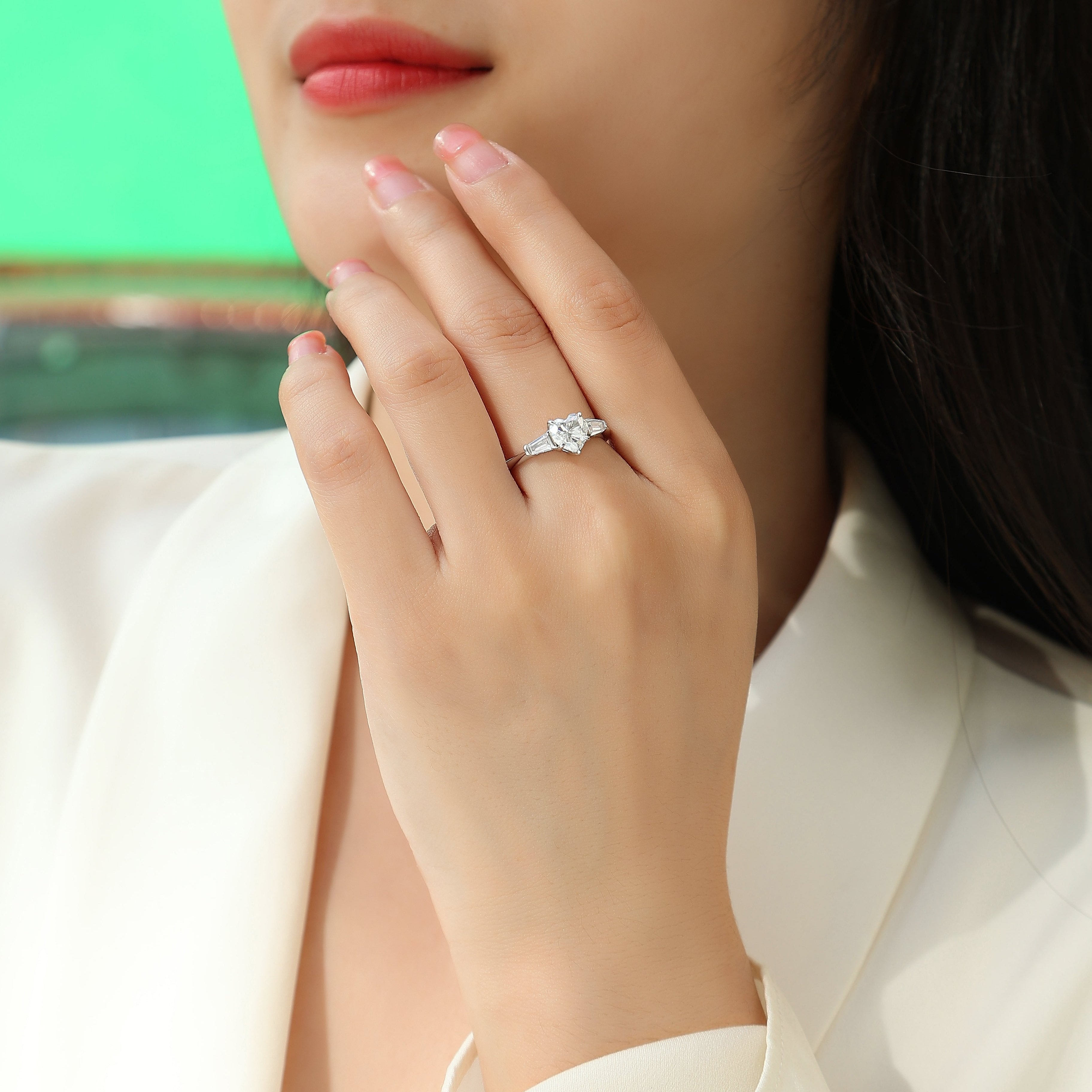 Three-stone moissanite ring on finger, heart-cut center with baguette side stones, white gold tone
