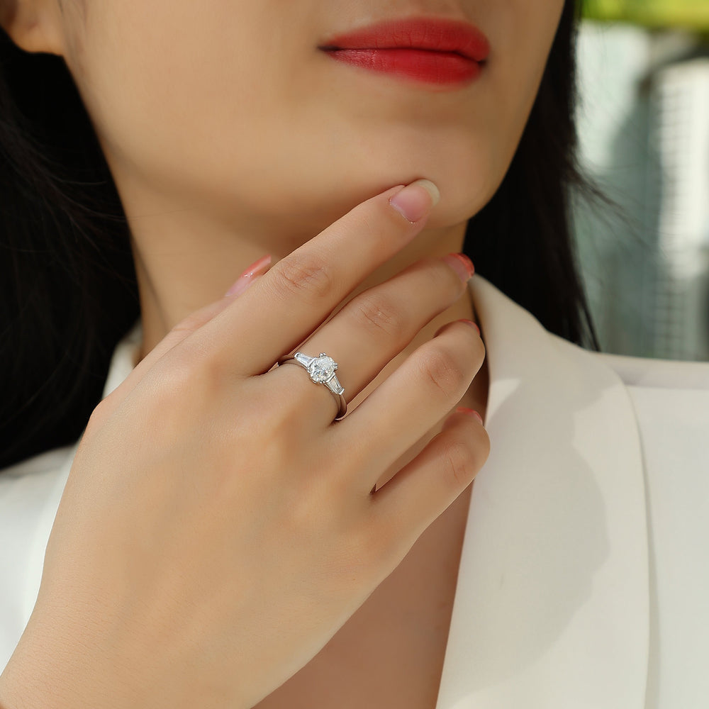 Ring on finger: oval moissanite center with baguette side stones, white gold band
