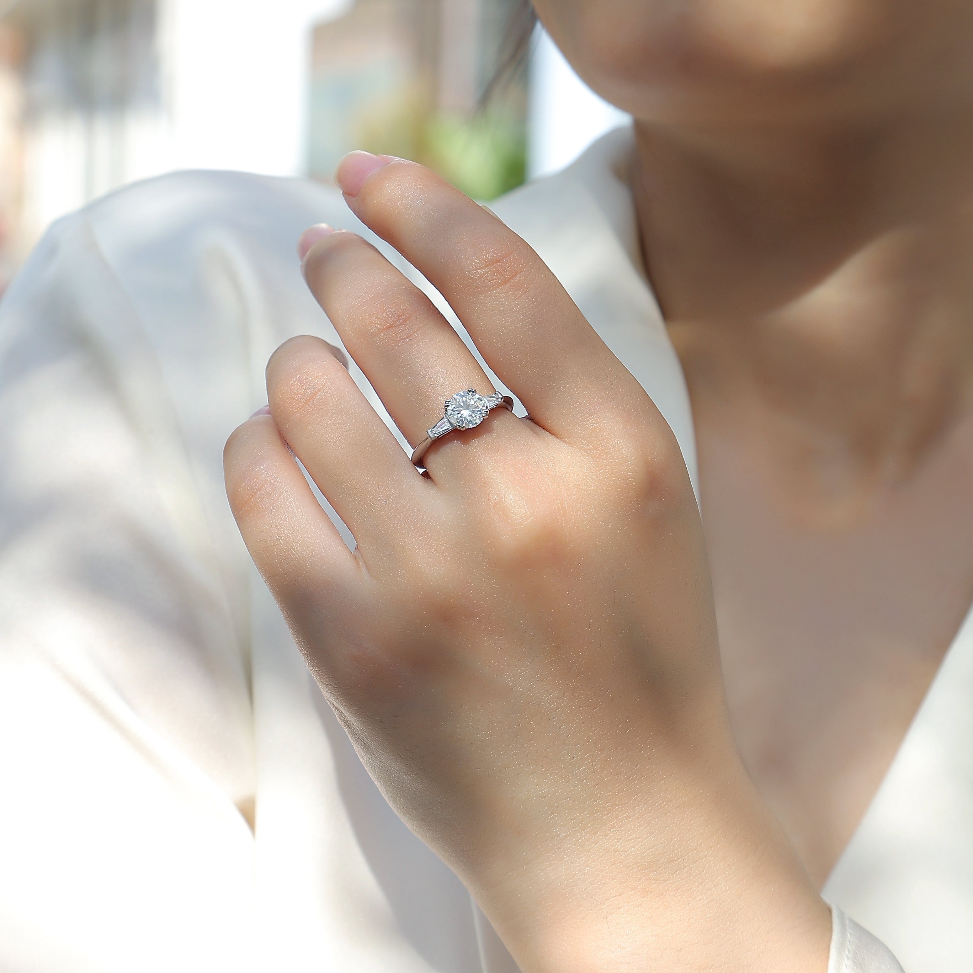 Round moissanite engagement ring on hand, white metal three-stone style