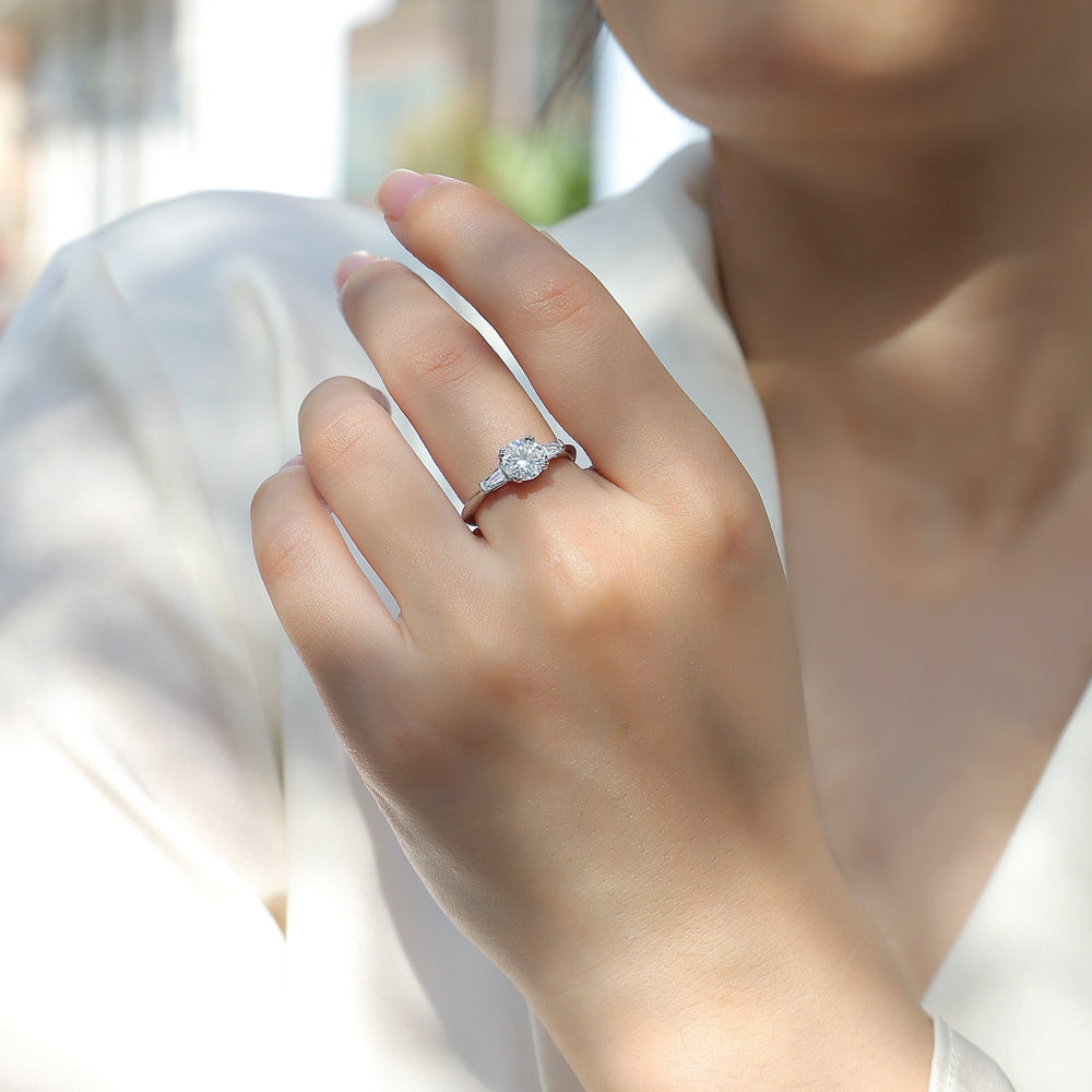 Round moissanite engagement ring on hand, white metal three-stone style