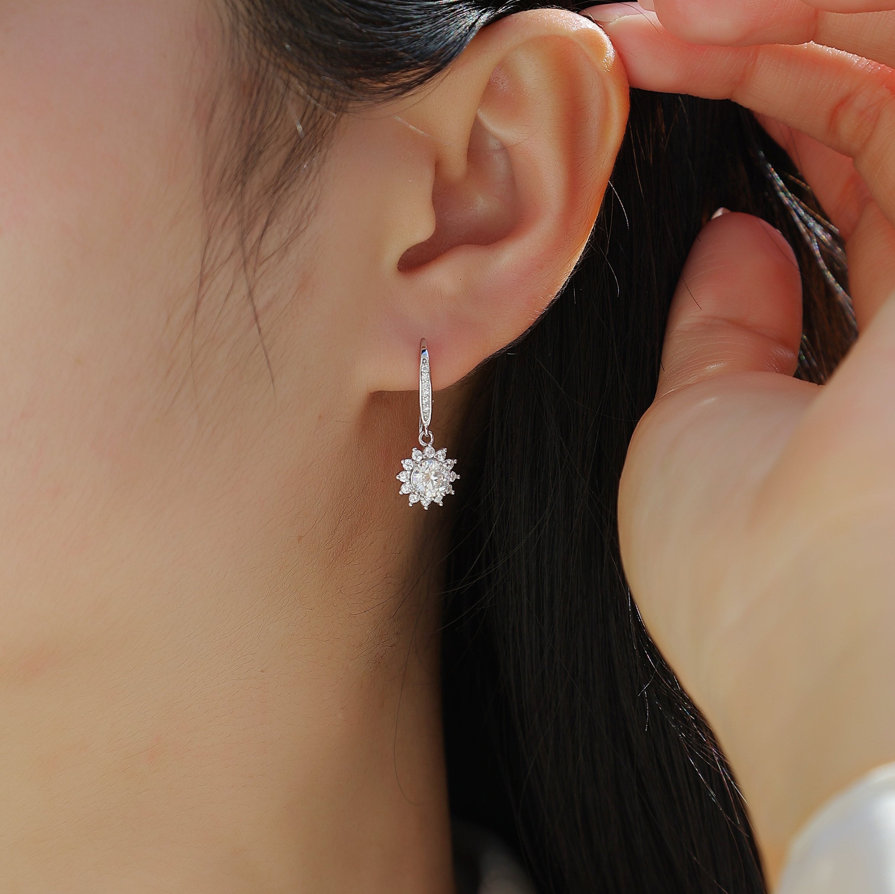 Sunflower halo drop earrings on ear, round moissanite center with small petal-like crystals