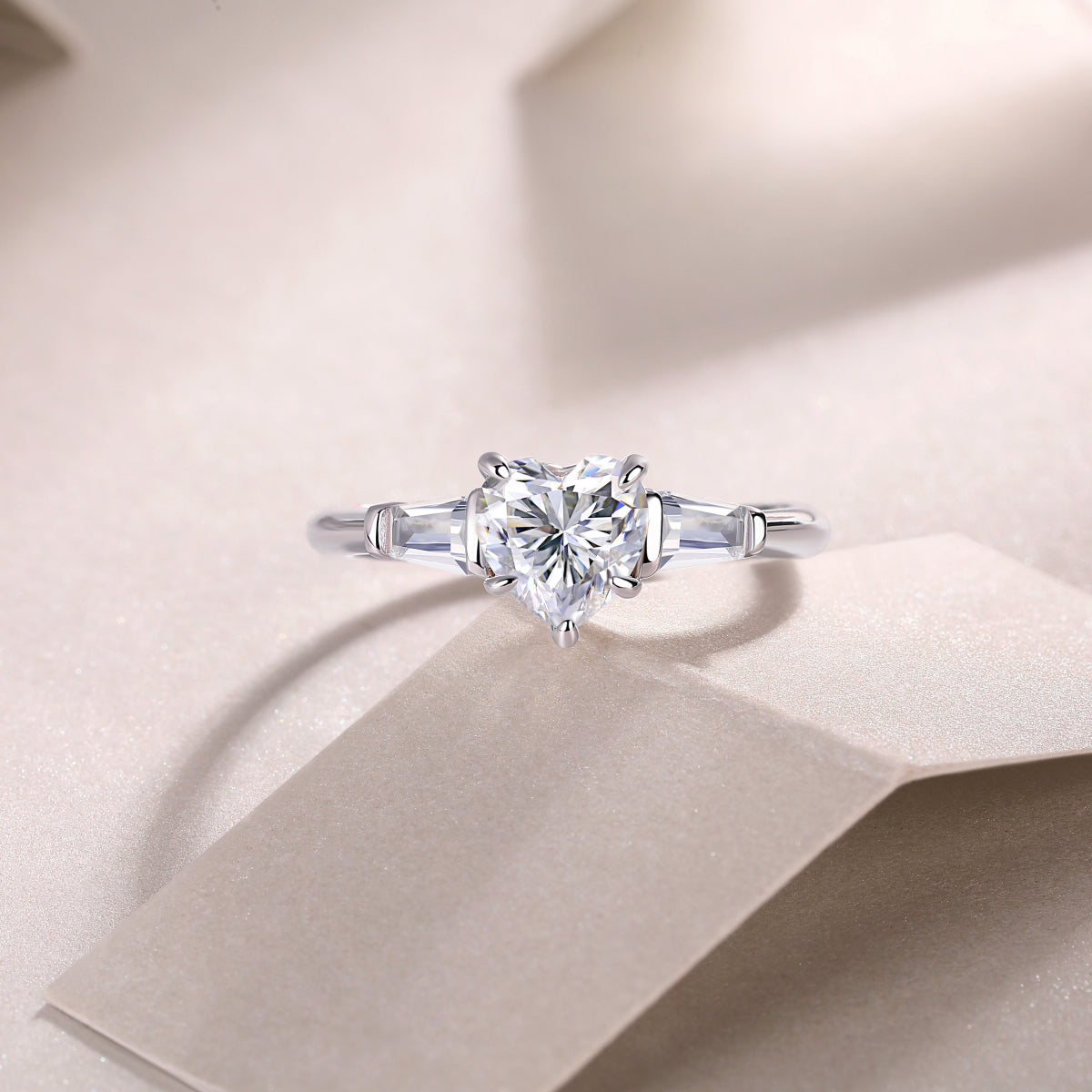 Three-stone heart-cut moissanite ring close-up on top, baguette side stones, white gold tone