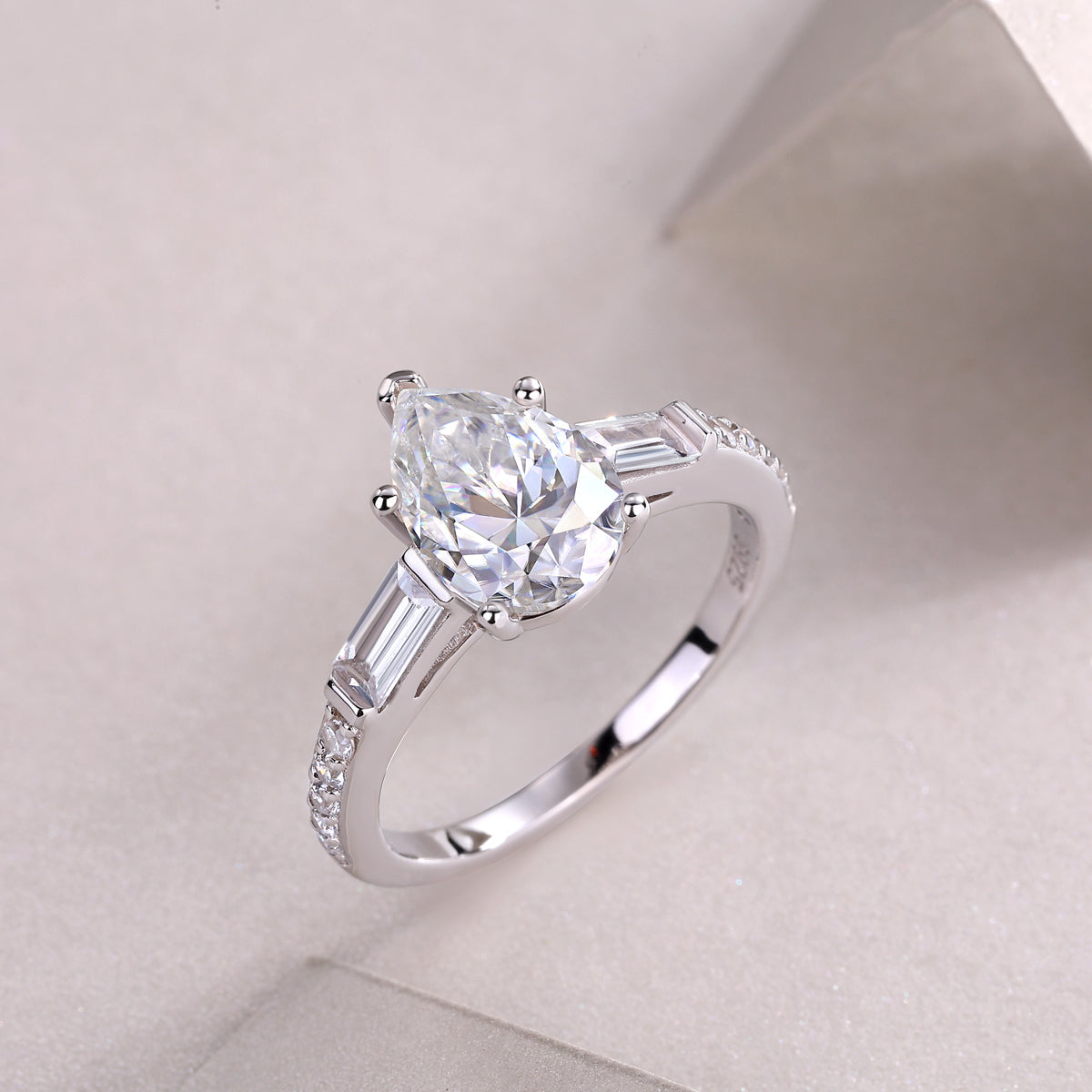 Side view of pear-cut moissanite ring, baguette accents and pavé band in white gold