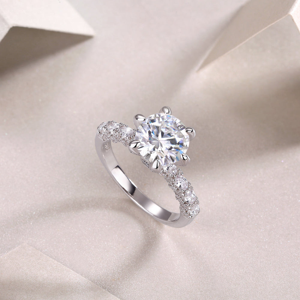 Angled view of six-prong pavé moissanite engagement ring with round center stone