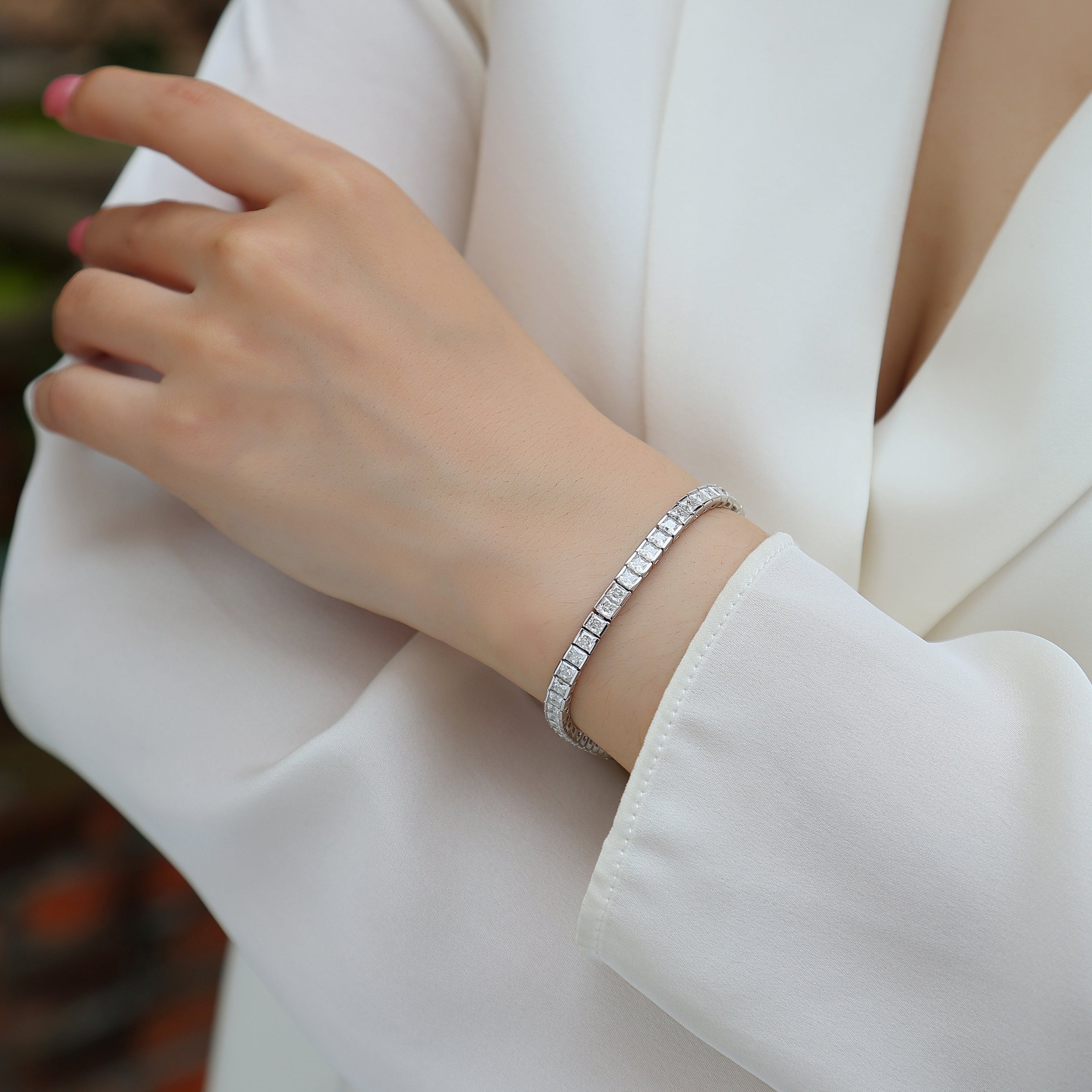 Princess cut moissanite tennis bracelet on wrist, thin silver-toned band with square stones