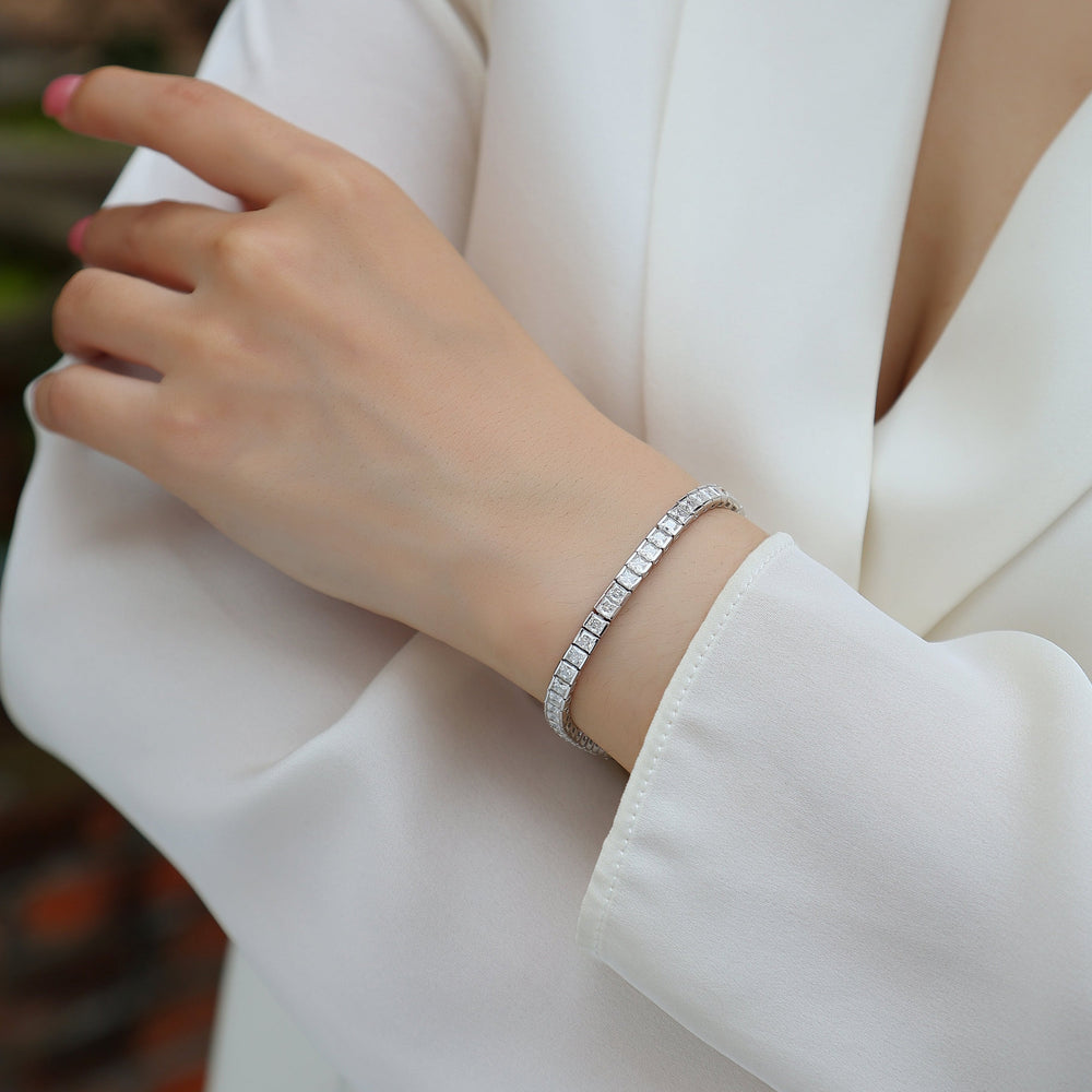Princess cut moissanite tennis bracelet on wrist, thin silver-toned band with square stones