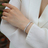 Princess cut moissanite tennis bracelet on wrist, thin silver-toned band with square stones