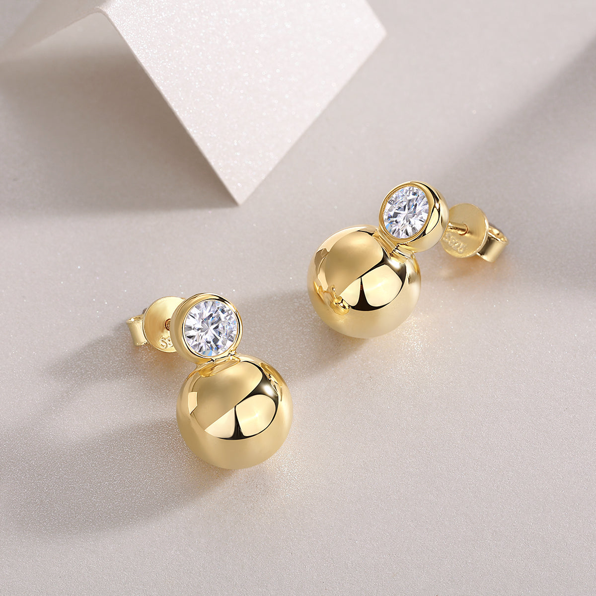 Angled view of bezel-set moissanite ball stud earrings in gold vermeil, polished finish