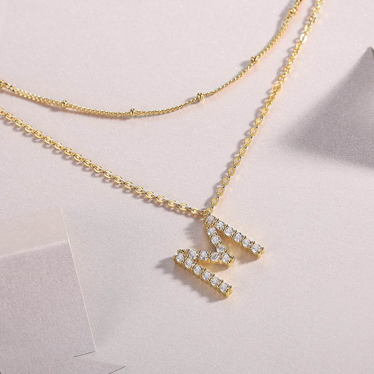 Close-up of double-layer M pendants with moissanite stones on gold chains