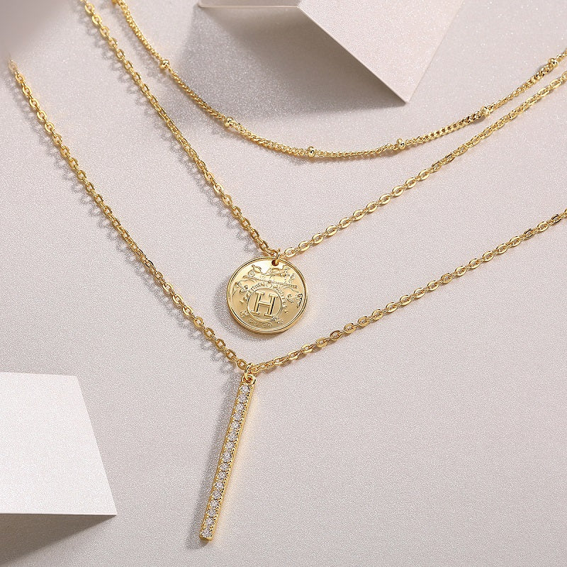 Layered necklace close-up: coin pendant and rhinestone bar charm, yellow gold vermeil