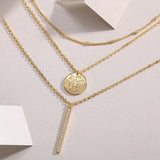 Layered necklace close-up: coin pendant and rhinestone bar charm, yellow gold vermeil