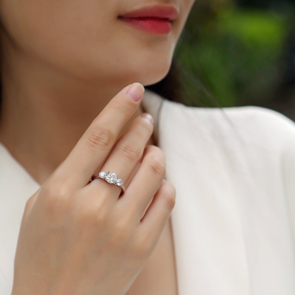 Round three-stone engagement ring on finger, white gold vermeil, prong-set moissanite