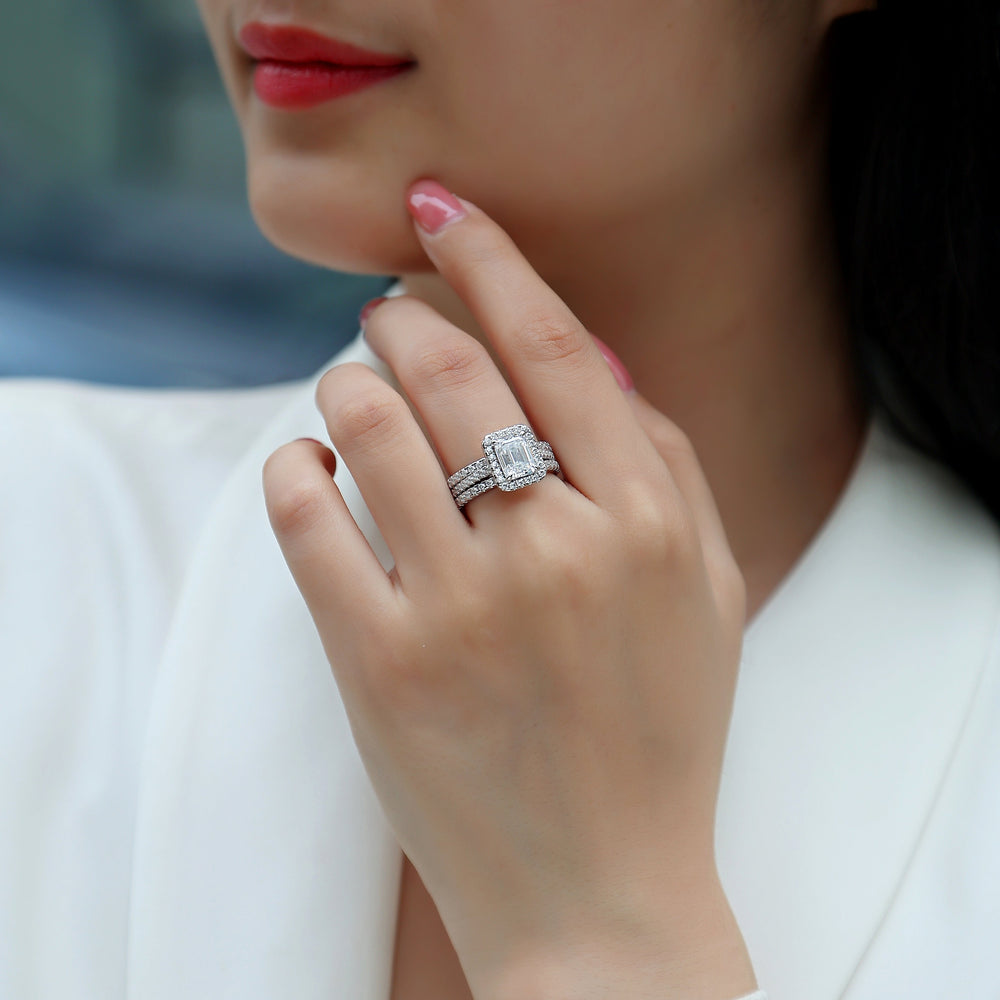 Emerald-cut halo ring set on finger with two stacked pavé bands, white gold vermeil