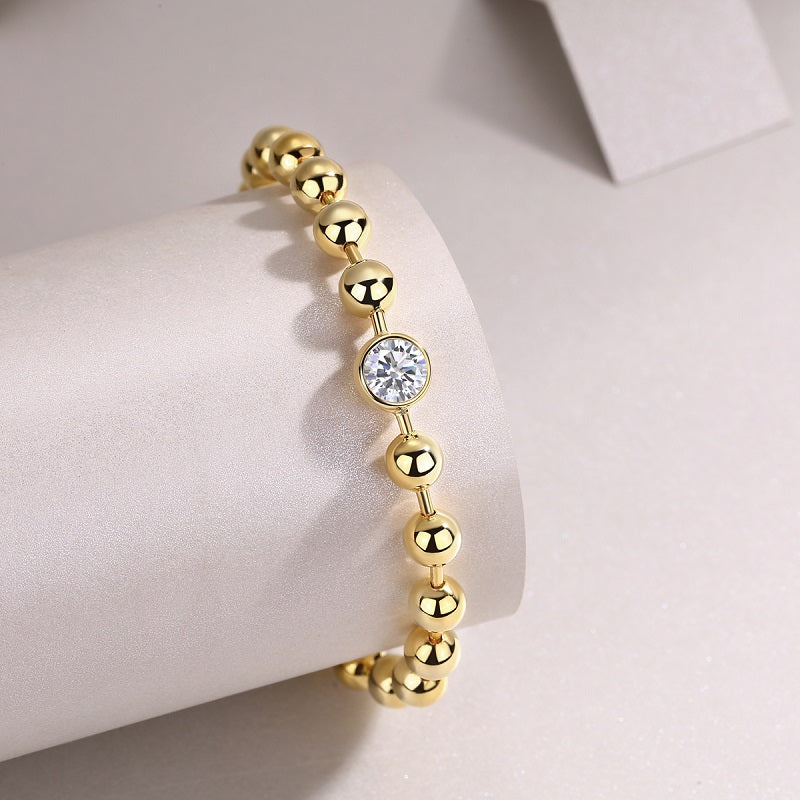 Bezel-set round moissanite stone on gold bead bracelet with toggle clasp detail
