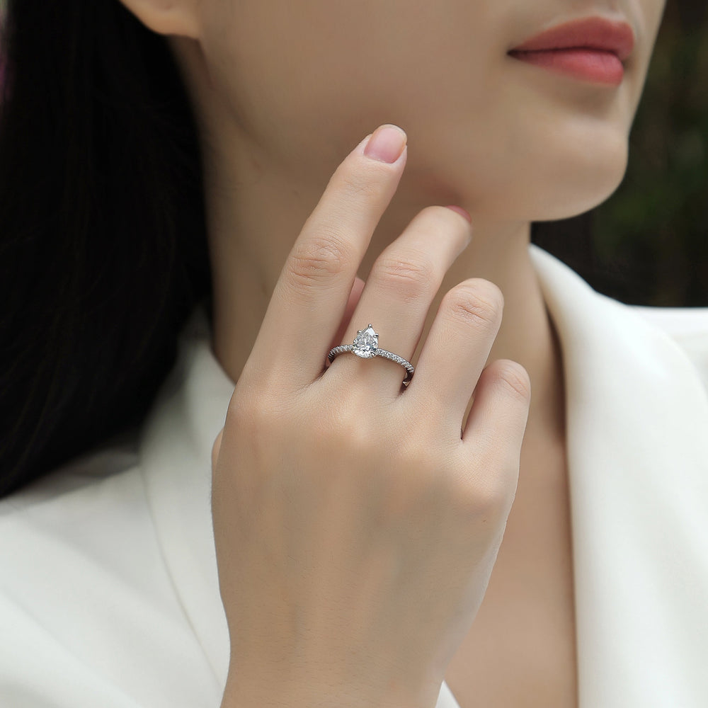 Pear cut pavé moissanite ring on finger, prong-set pear center with pavé band
