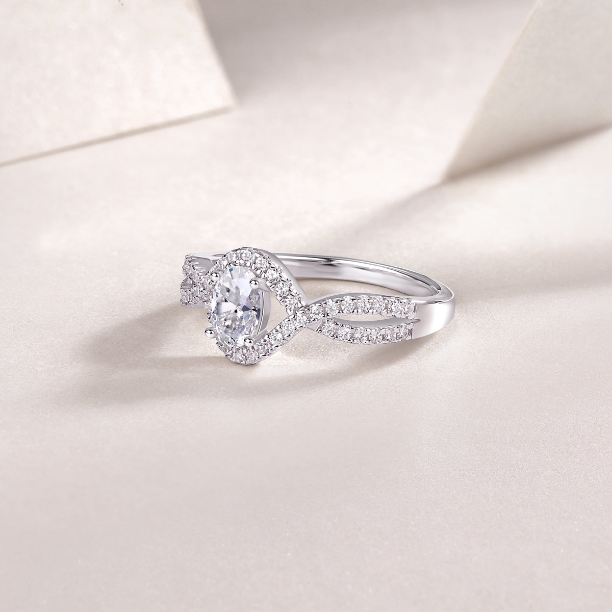 Angled view of oval halo moissanite ring with twisted pavé band, white gold vermeil