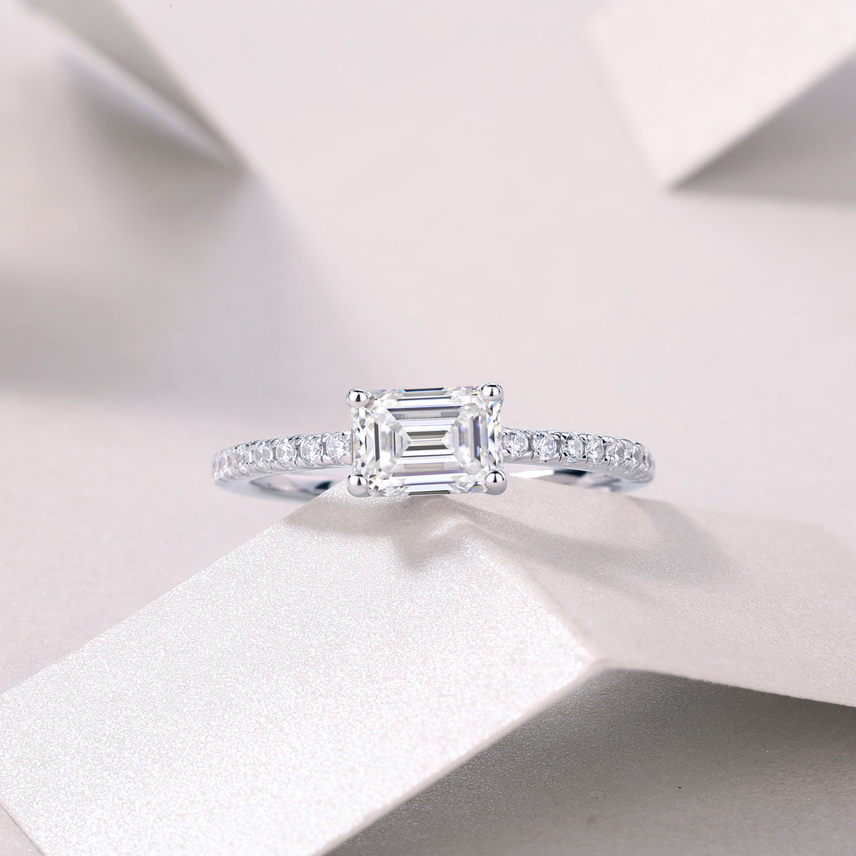 Emerald-cut moissanite ring with pavé shoulders, white gold tone, angled front view
