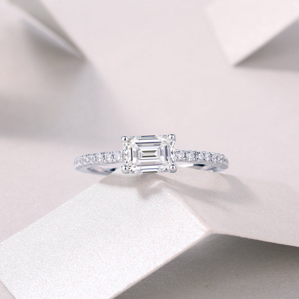 Emerald-cut moissanite ring with pavé shoulders, white gold tone, angled front view