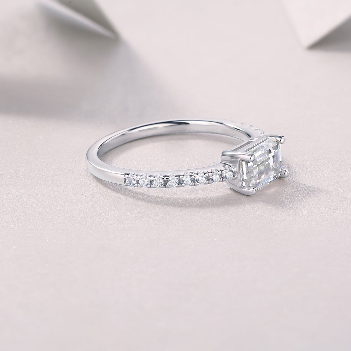 Side profile of emerald-cut moissanite ring with pavé band, white gold tone
