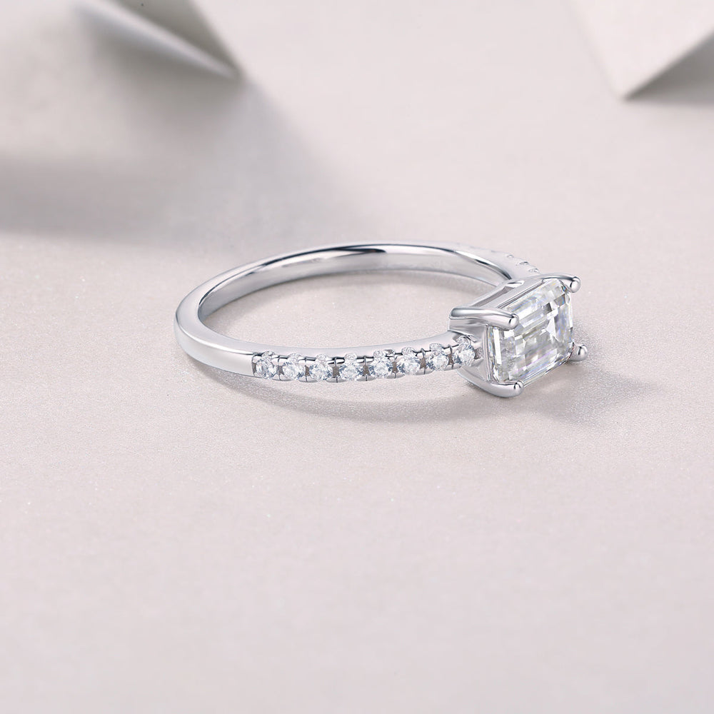 Side profile of emerald-cut moissanite ring with pavé band, white gold tone