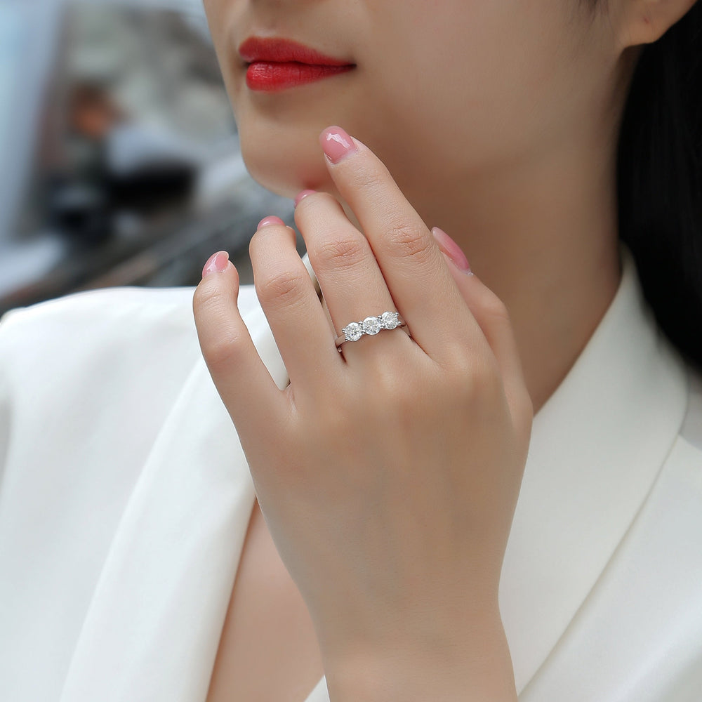 Three-stone moissanite ring on finger, white gold vermeil band with round stones