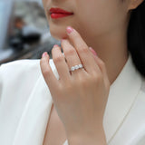 Three-stone moissanite ring on finger, white gold vermeil band with round stones